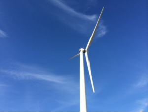 Upward view of a large white wind turbine with a clear blue sky.